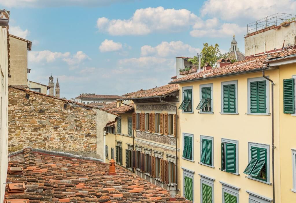 Eine enge Straße mit terrakottafarbenen Dächern und traditionellen Gebäuden mit grünen Fensterläden.