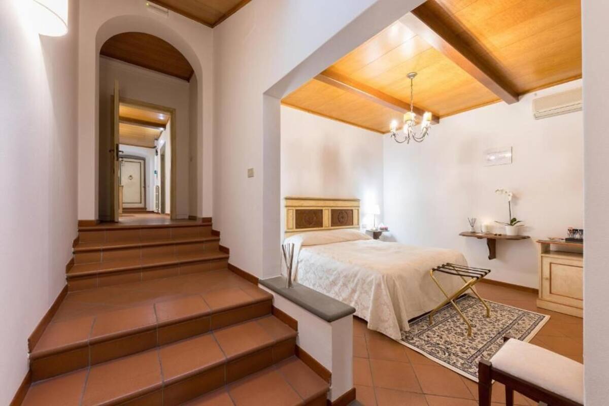 Une chambre à coucher avec un lit, une table de chevet, un lustre et une salle de bain visible à travers une arche.
