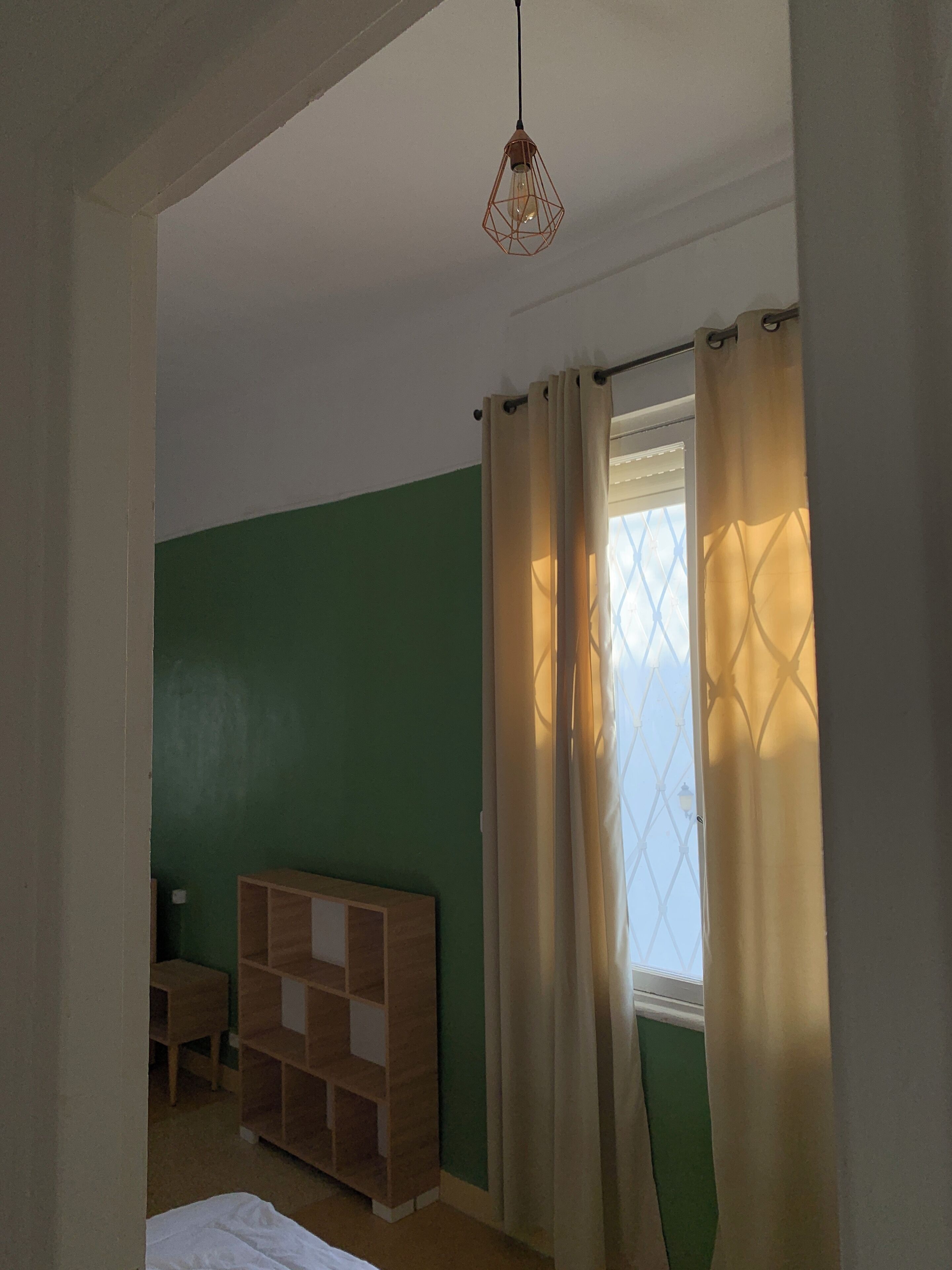Une pièce comprenant un lit, une armoire en bois, une fenêtre avec des rideaux et un luminaire suspendu.