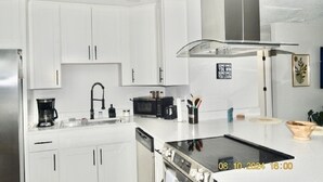 Una cocina moderna con armarios blancos, una campana extractora de acero inoxidable, un microondas y una cafetera.