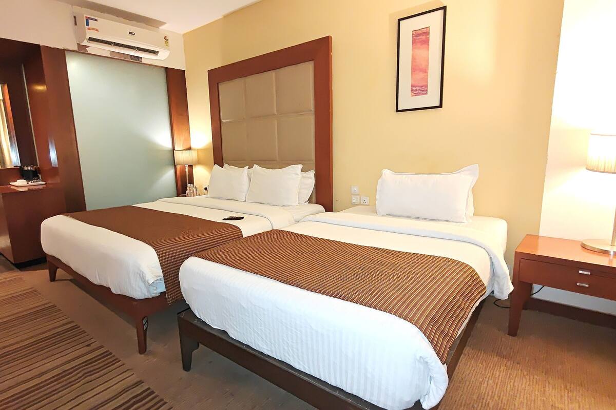 Een hotelkamer met twee bedden, een bureau, een lamp en een airconditioner.