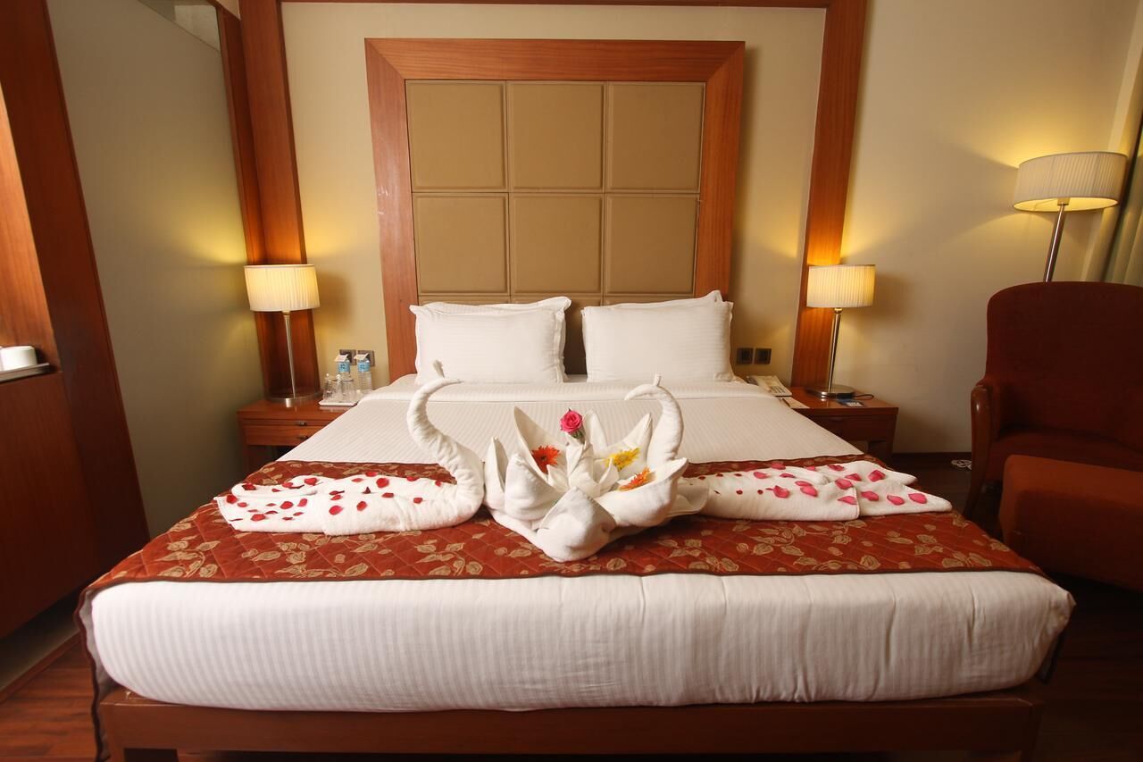 A hotel room with a large bed, two bedside tables, a wooden headboard, and two lamps.
