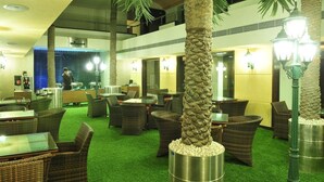Een hotellobby met rieten meubels, palmbomen en een groen tapijt.