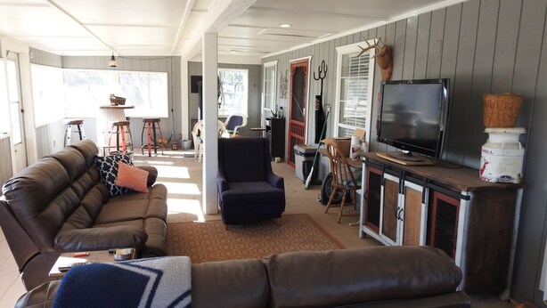 A cozy living room with a leather sofa, a dark armchair, and a TV on a wooden cabinet. - Mason Ranch Guest House (Mason)