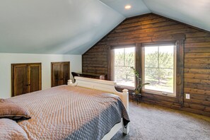 A bedroom with a sloped ceiling, a large window, a bed, and wooden walls. - Deck & Fire Pit! Quiet Home Near Sacramento River (Glenn)