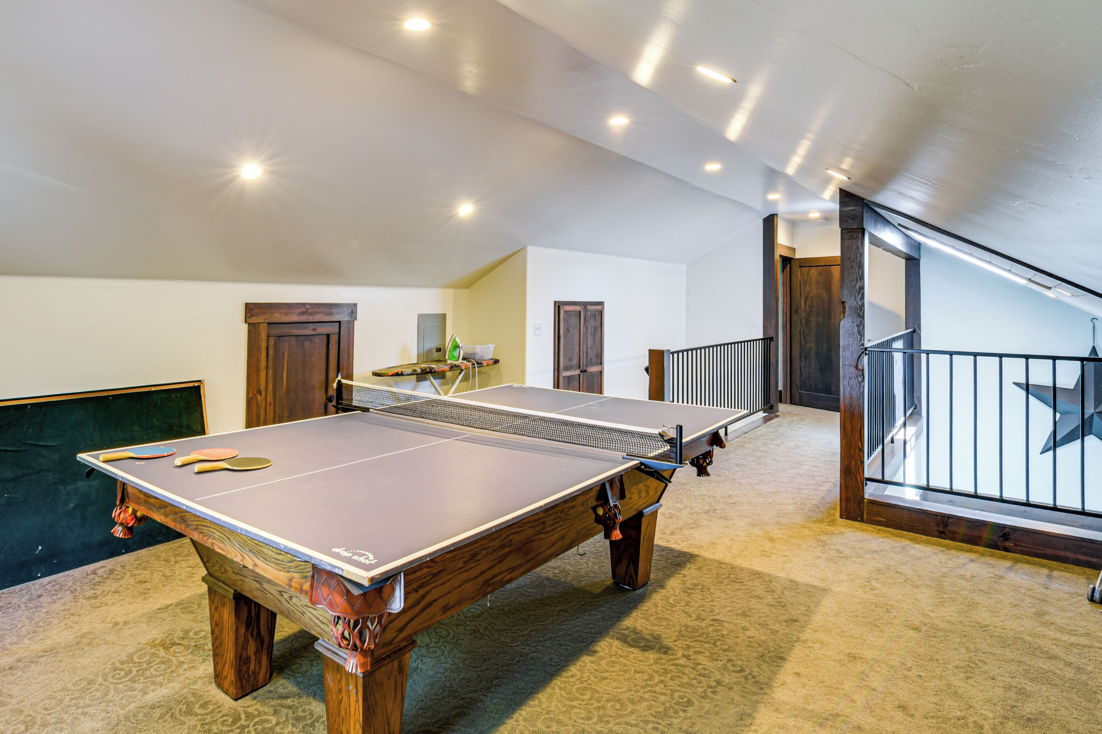 A ping pong table in a room with a carpeted floor, wooden doors, and a staircase with a railing.