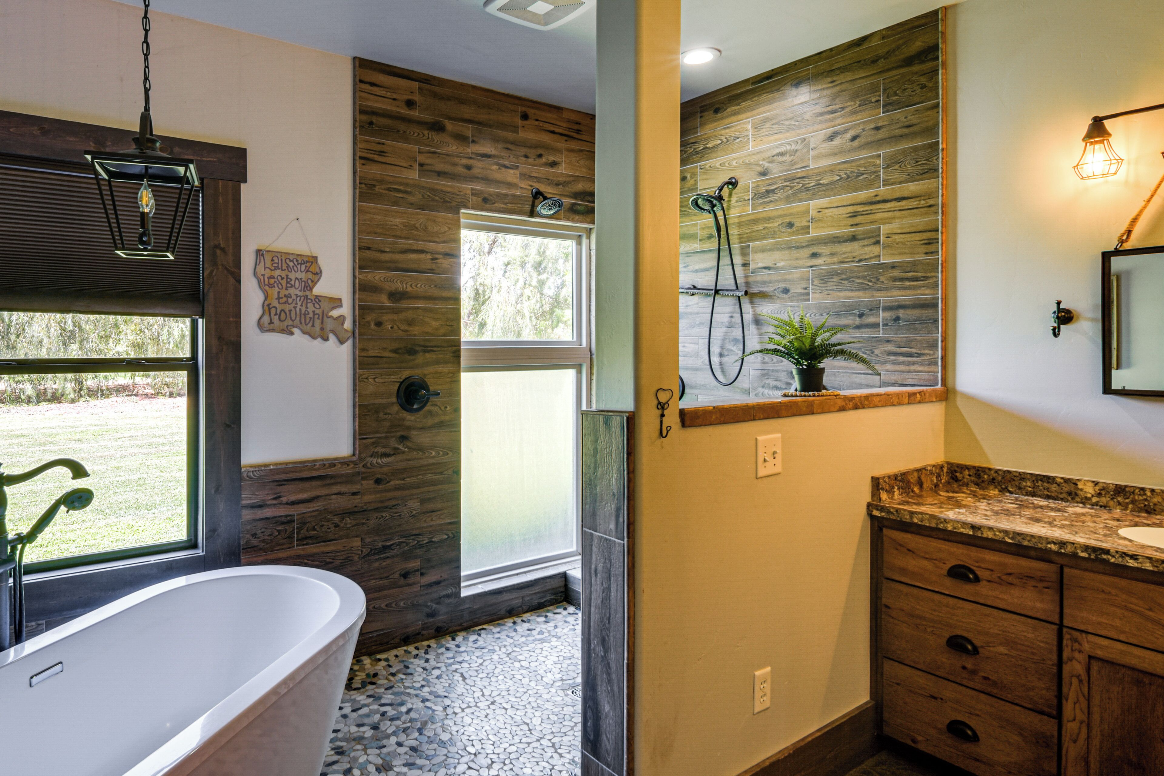 A bathroom with a freestanding bathtub, a shower with a wooden wall, and a sink with a granite countertop.