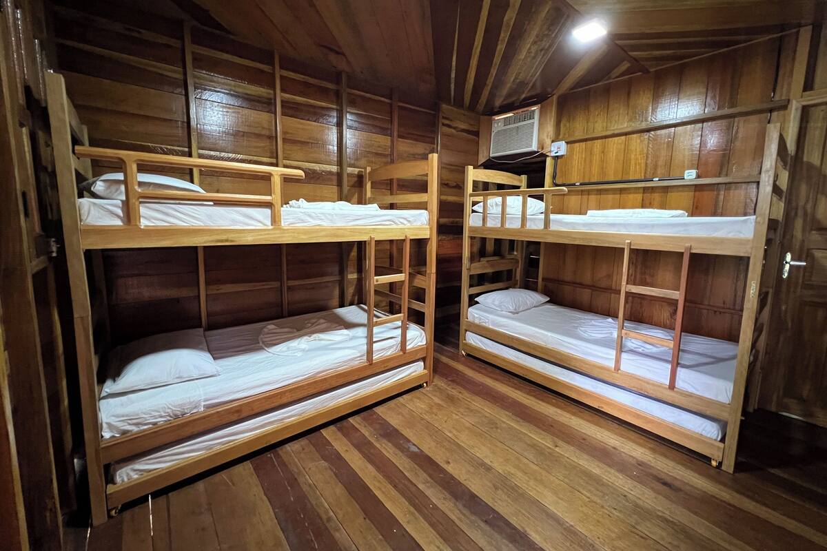 A room with two bunk beds, wooden walls, a ceiling fan, and a door.