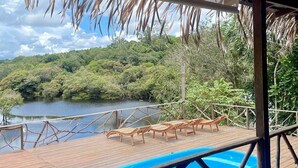 A wooden deck with a pool, lounge chairs, and a view of a lake surrounded by trees. - Pousada Cabana Nativa Paraíso (Careiro)