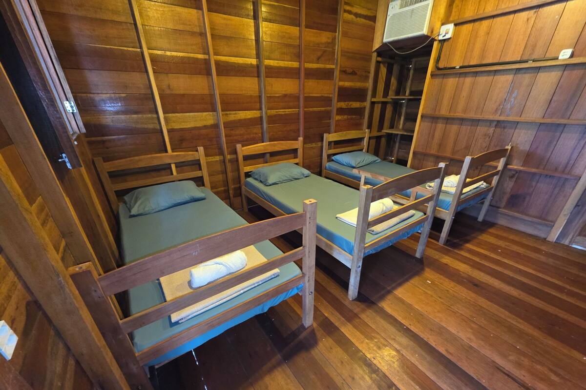 A room with four wooden bunk beds, a wooden floor, and a wall-mounted air conditioning unit.