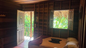 Una habitación de cabaña de madera con cama, ventana con contraventanas y puerta.
