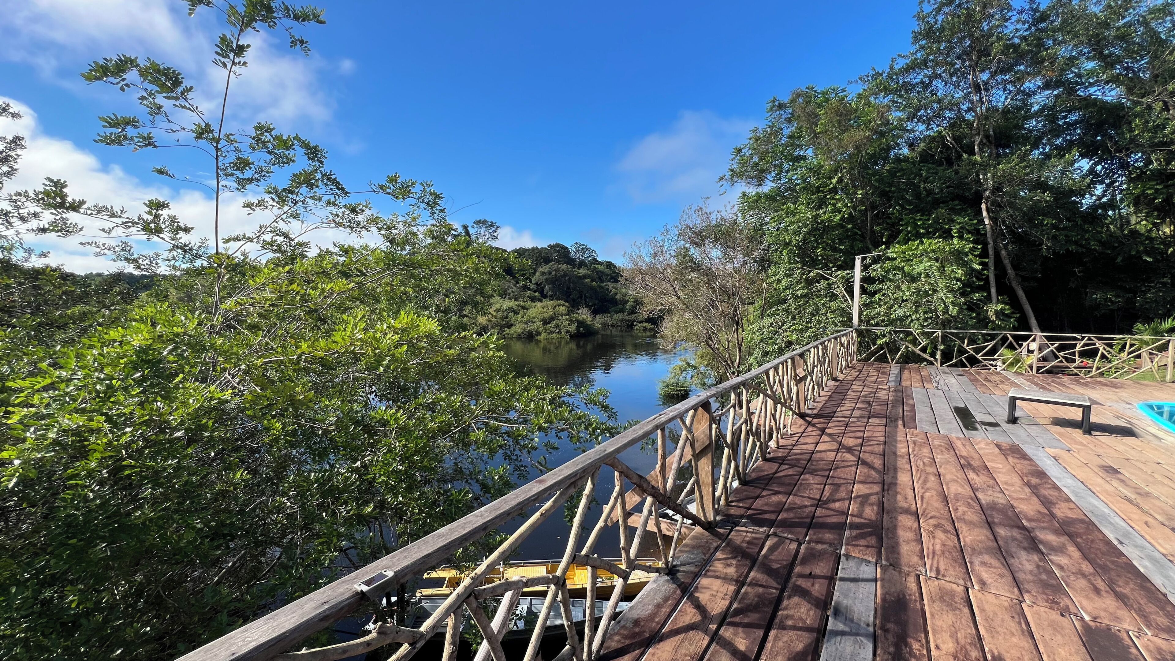 Eine Holzbrücke mit Geländern und einer Holzterrasse, mit Blick auf einen von Grünflächen gesäumten Fluss.