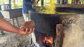 A hand holding a piece of bread over a large cooking pot with flames underneath.