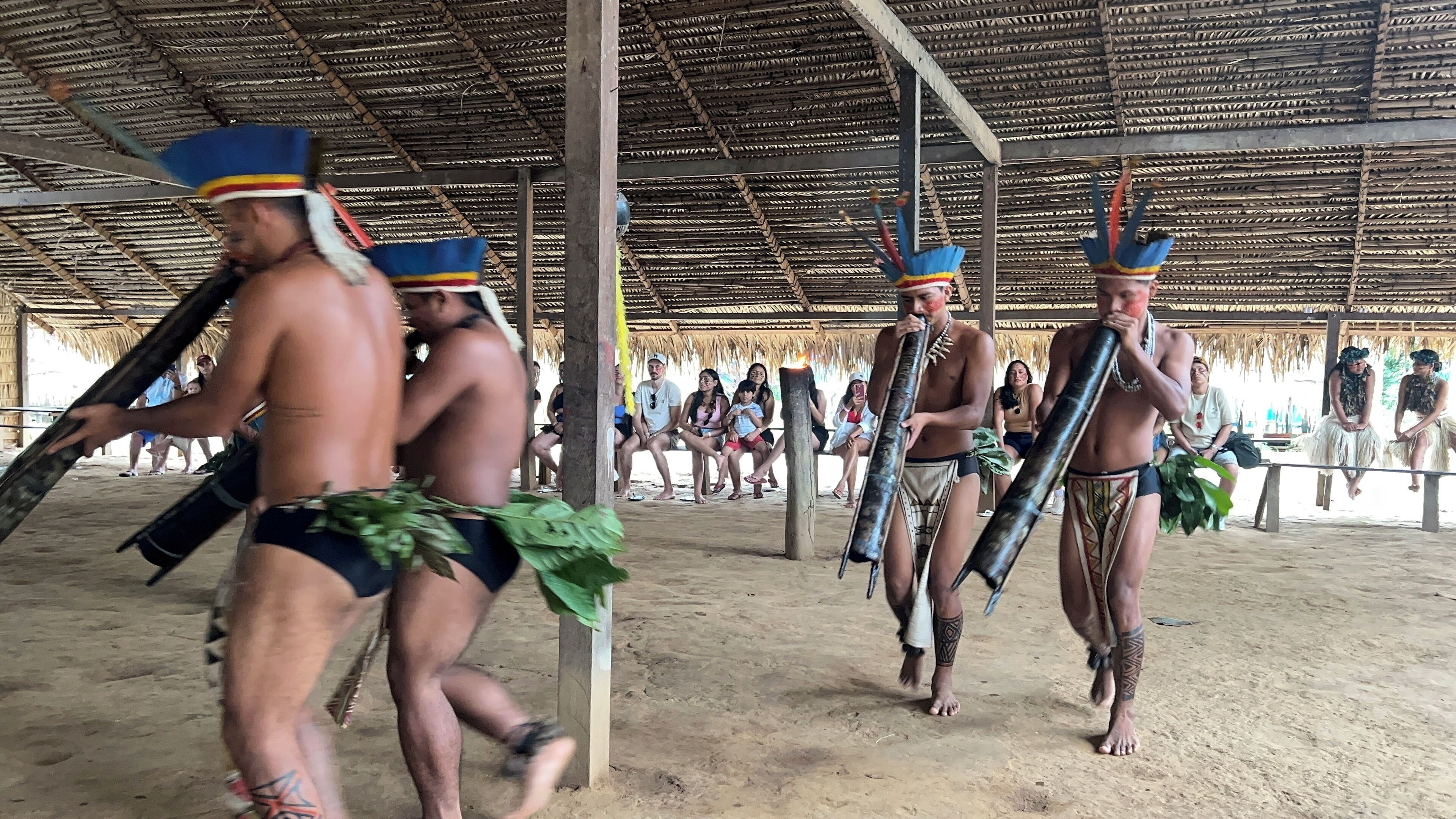 A group of people in traditional attire under a thatched roof structure.