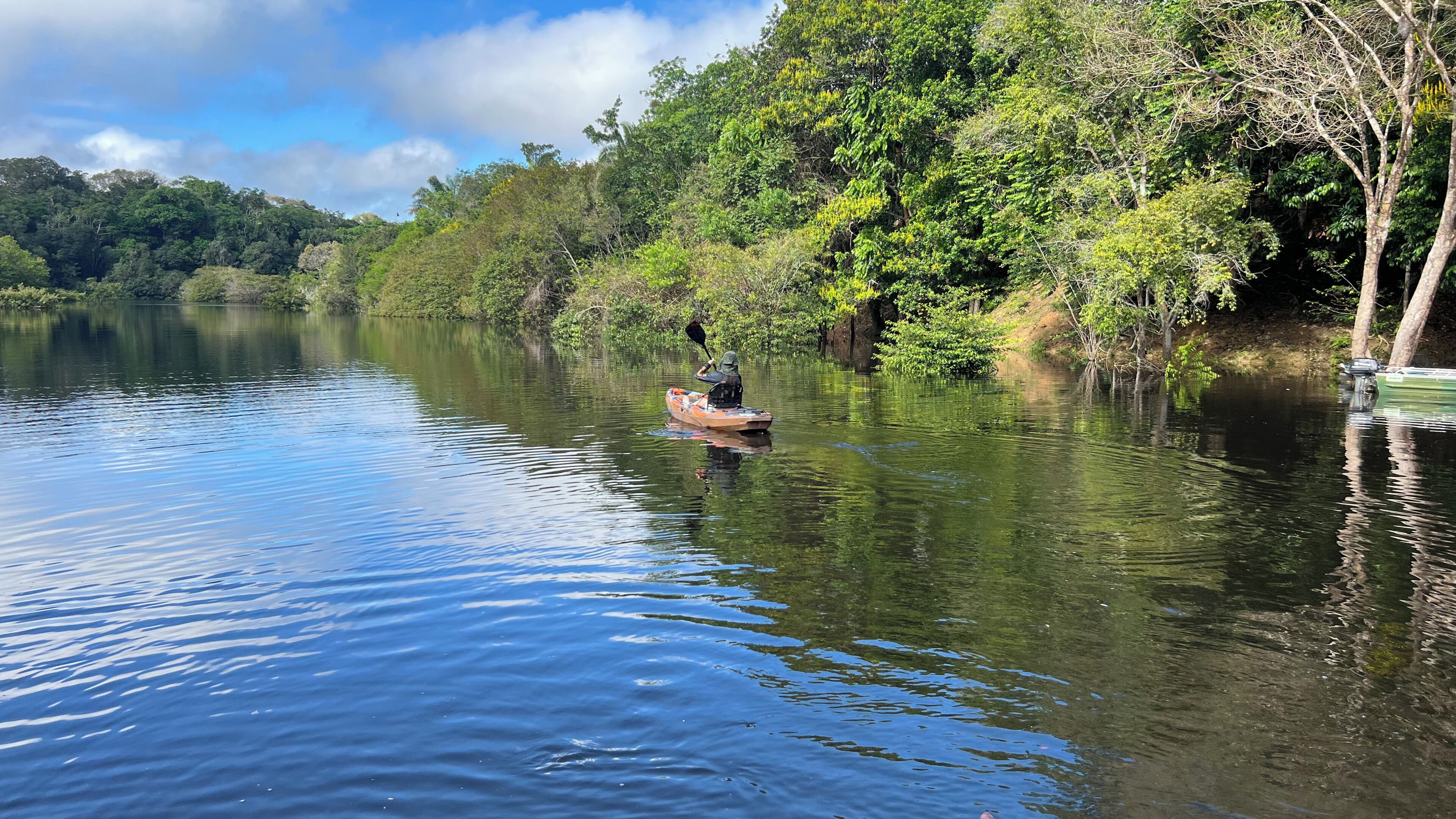 A calm river with a small boat and dense greenery on the banks.