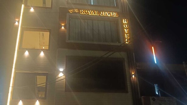 Um edifício de vários andares com sinalização iluminada que diz "The Royal Jewel Hotel" e "The Royal Jewel".