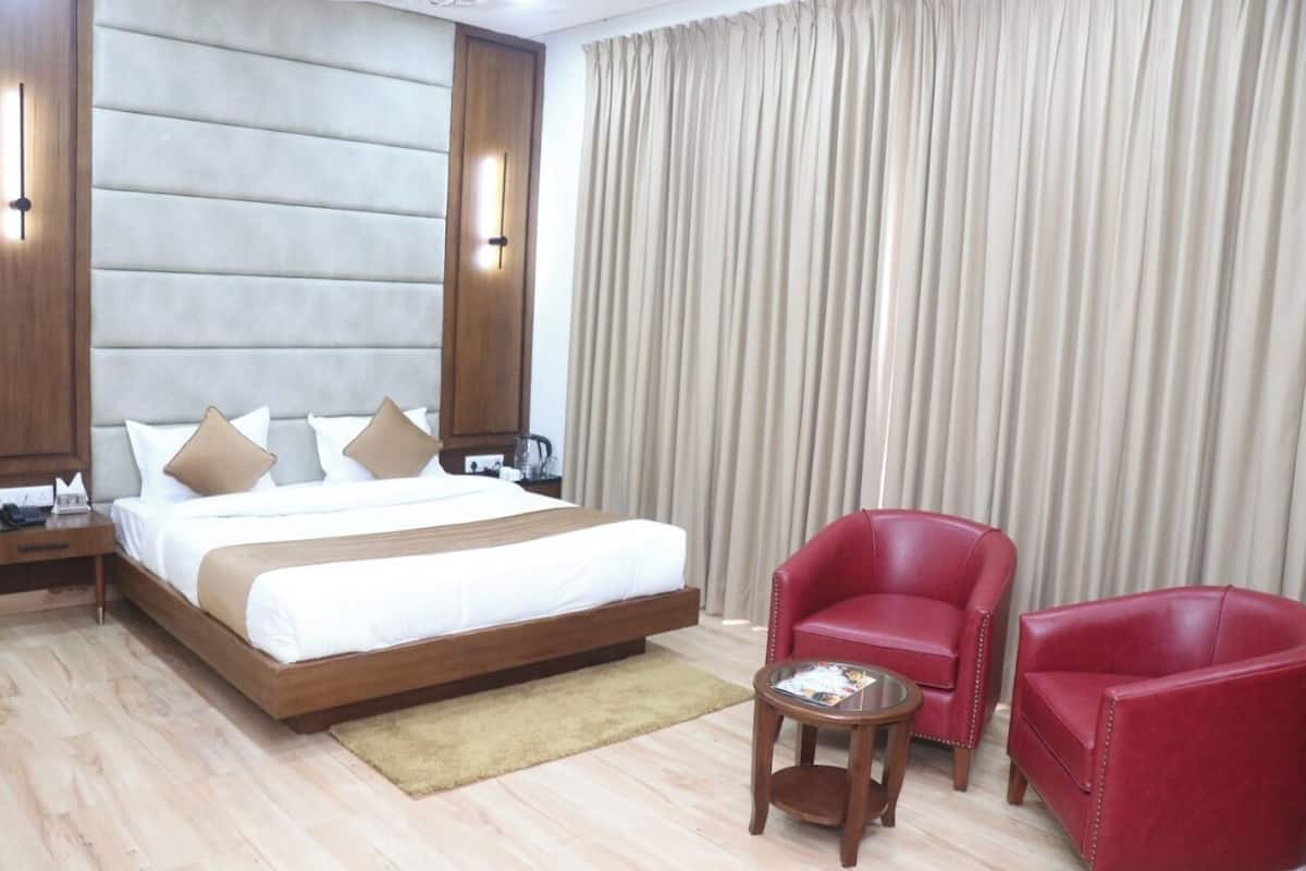 Une chambre d’hôtel avec un grand lit, deux fauteuils rouges, une petite table et un rideau.