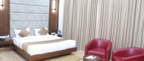 A hotel room with a large bed, two red chairs, a small table, and a curtain.
