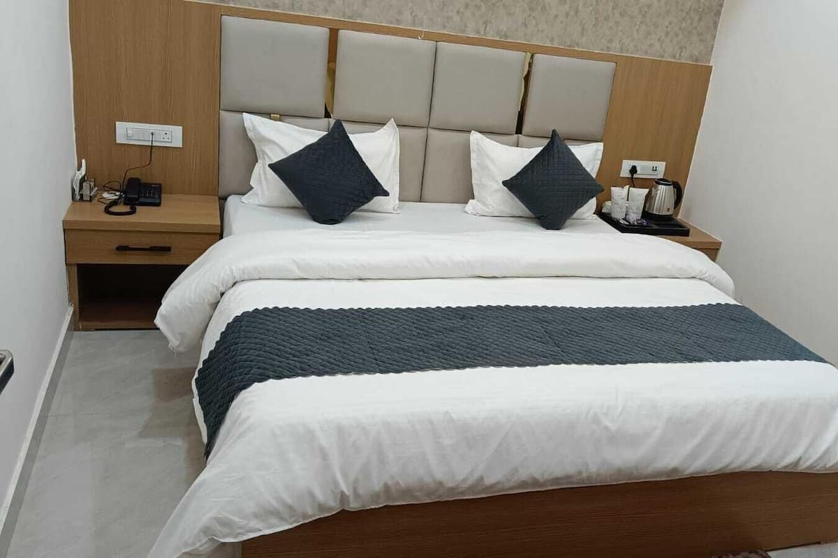 Une chambre d’hôtel comprenant un lit, deux tables de chevet, une petite table, une prise de courant et une machine à café.