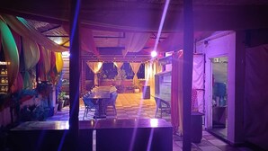 Um espaço interno com piso xadrez, uma mesa central com cadeiras e teto decorado com tecido pendurado.
