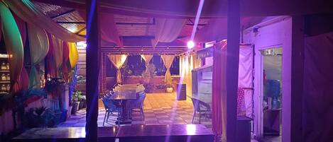 Un espacio interior con piso a cuadros, una mesa central con sillas y un techo cubierto de tela.