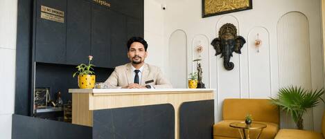 A reception desk with a 'No Smoking' sign, a receptionist, and a reception area with a sofa and decorative wall art.
