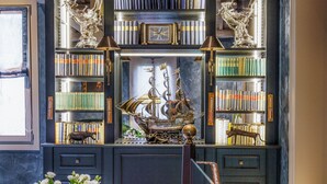 Ein Zimmer mit einer Bücherwand voller Bücher und Dekorationsobjekten, einem violetten Sofa und einem Fenster mit natürlichem Licht.