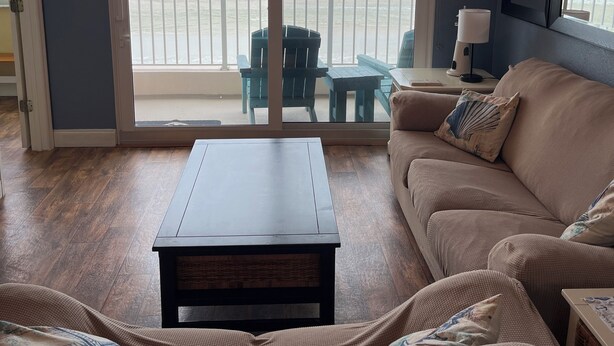 Un salon avec vue sur l’océan, un ventilateur de plafond, un canapé, une table basse et un balcon aménagé avec du mobilier d’extérieur.