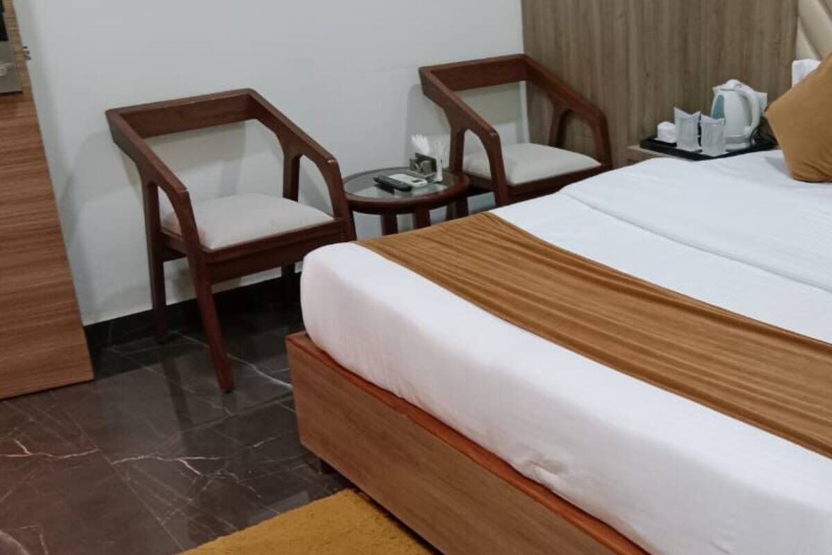 Une chambre d’hôtel avec un grand lit, deux chaises en bois, une petite table avec une bouilloire et une table de chevet.