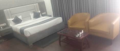 Una habitación de hotel con una cama, dos sillones, una mesita y una mesita de noche.