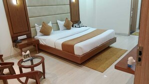 Une chambre d’hôtel avec un grand lit, une tête de lit en bois, des tables de chevet, une table ronde et un petit coin salon.