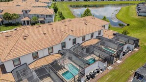 Un ensemble résidentiel comprenant plusieurs maisons dotées de toits en tuiles et d’un espace piscine agrémenté de zones protégées par des parois de verre.