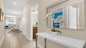 A modern hallway with a white console table, a mirror, and a potted orchid. - Cozy 5BD Home Paradise Palms Resort with Pool (Kissimmee)