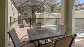 A covered outdoor patio with a pool, seating area, and a table. - Cozy 5BD Home Paradise Palms Resort with Pool (Kissimmee)
