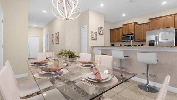 A modern kitchen with wooden cabinets, stainless steel appliances, and a glass dining table set for six. - Cozy 5BD Home Paradise Palms Resort with Pool (Kissimmee)