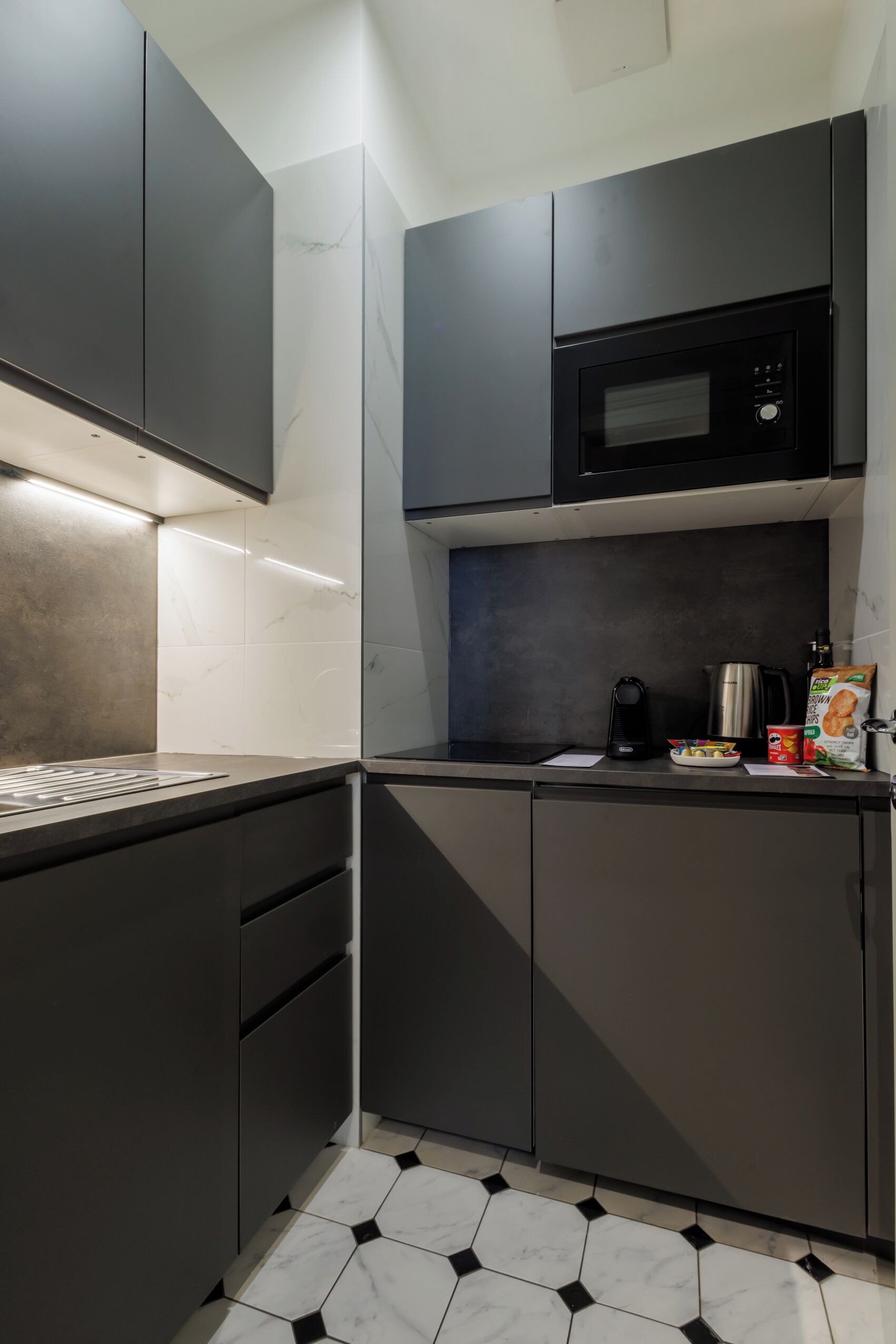 Una cucina moderna con mobili scuri, un forno a microonde, un bollitore e una macchina per il caffè.