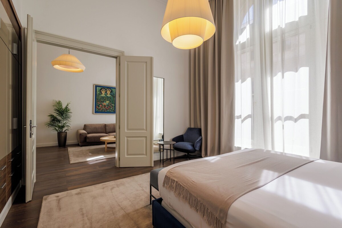 Une chambre d’hôtel avec un lit, un canapé, une chaise, une plante en pot et un tableau au mur.