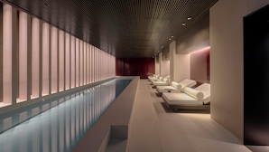 Un spa moderne doté d’une longue piscine, de chaises longues et d’un plafond orné de motifs.