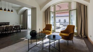 Une chambre d’hôtel moderne dotée d’un coin repas, de deux fauteuils, d’une table basse et d’une grande fenêtre avec des rideaux.