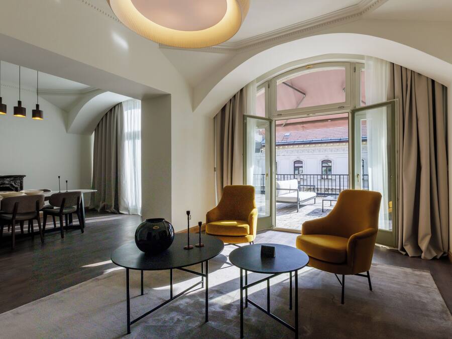 Une chambre d’hôtel moderne dotée d’un coin repas, de deux fauteuils, d’une table basse et d’une grande fenêtre avec des rideaux.