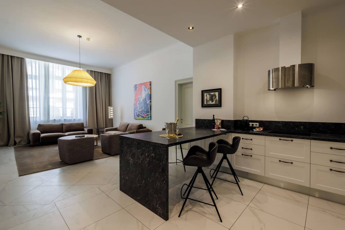 Una cocina moderna con una isla de mármol, taburetes negros, una lámpara colgante y una zona de comedor con sofá y una mesa de centro.