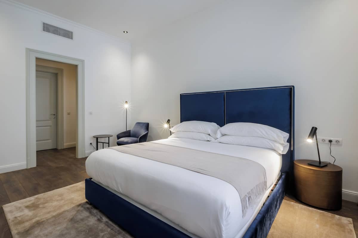Un dormitorio con una cama, mesitas de noche, una silla y una lámpara.