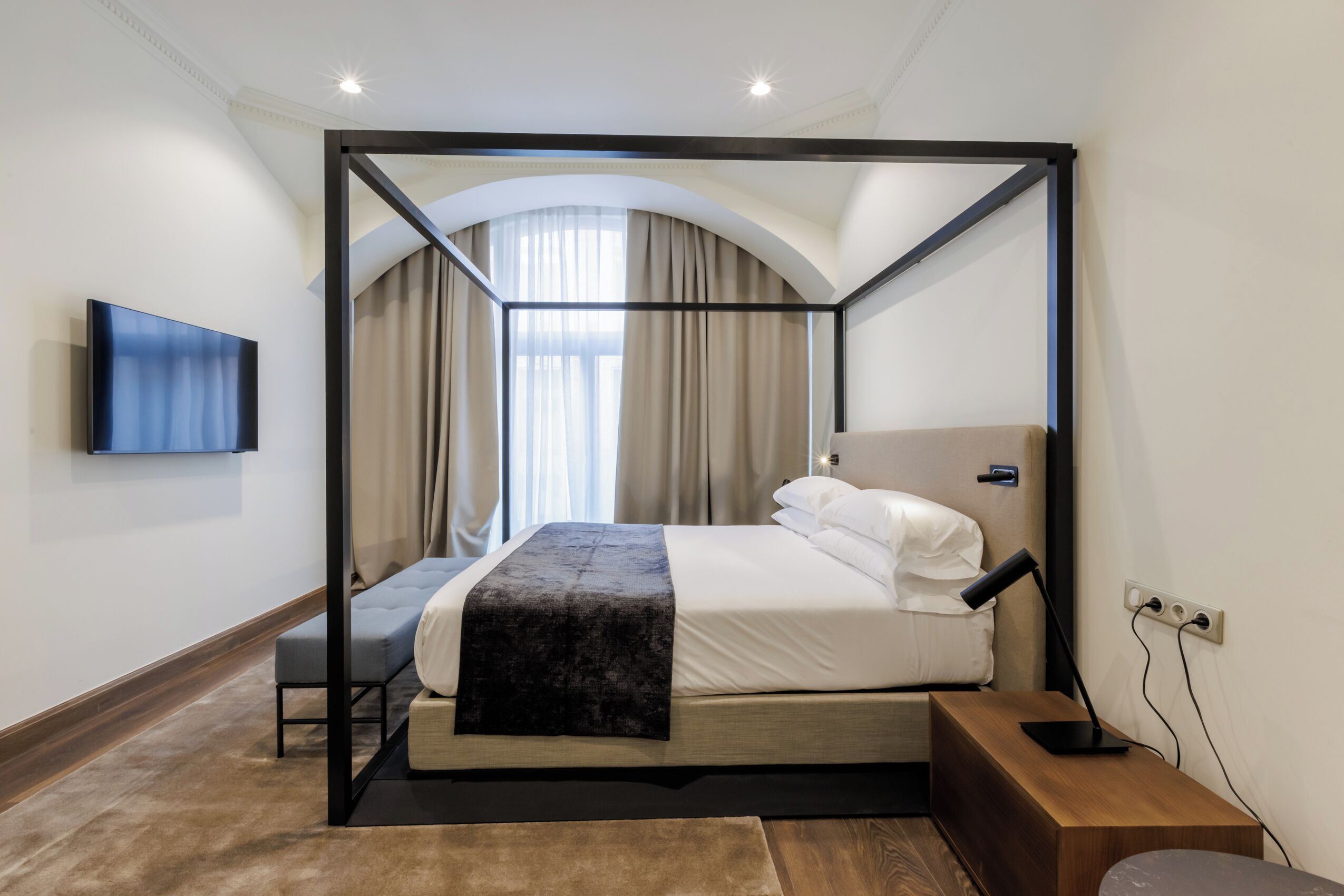 A four-poster bed with a flat-screen TV, a bedside table, and a power outlet.
