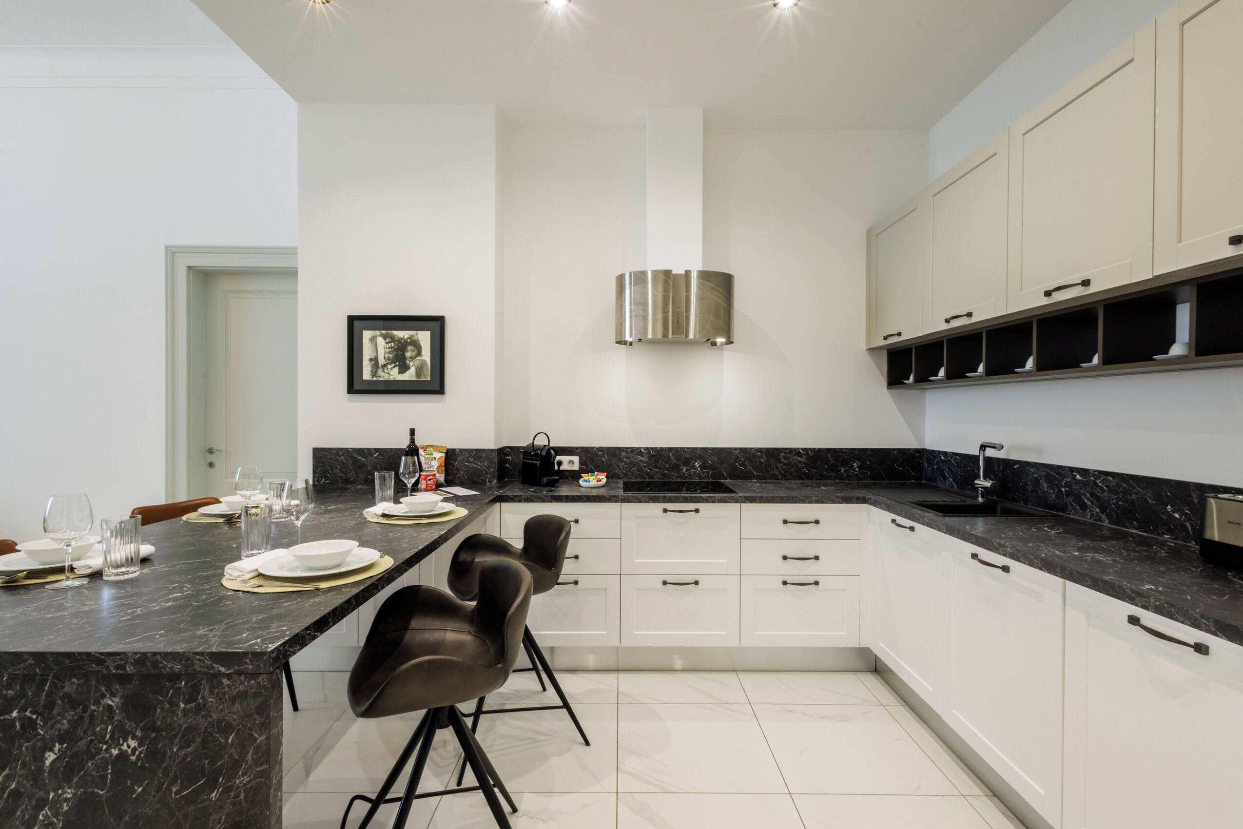 A modern kitchen with a marble countertop, white cabinets, and a central island with bar stools.