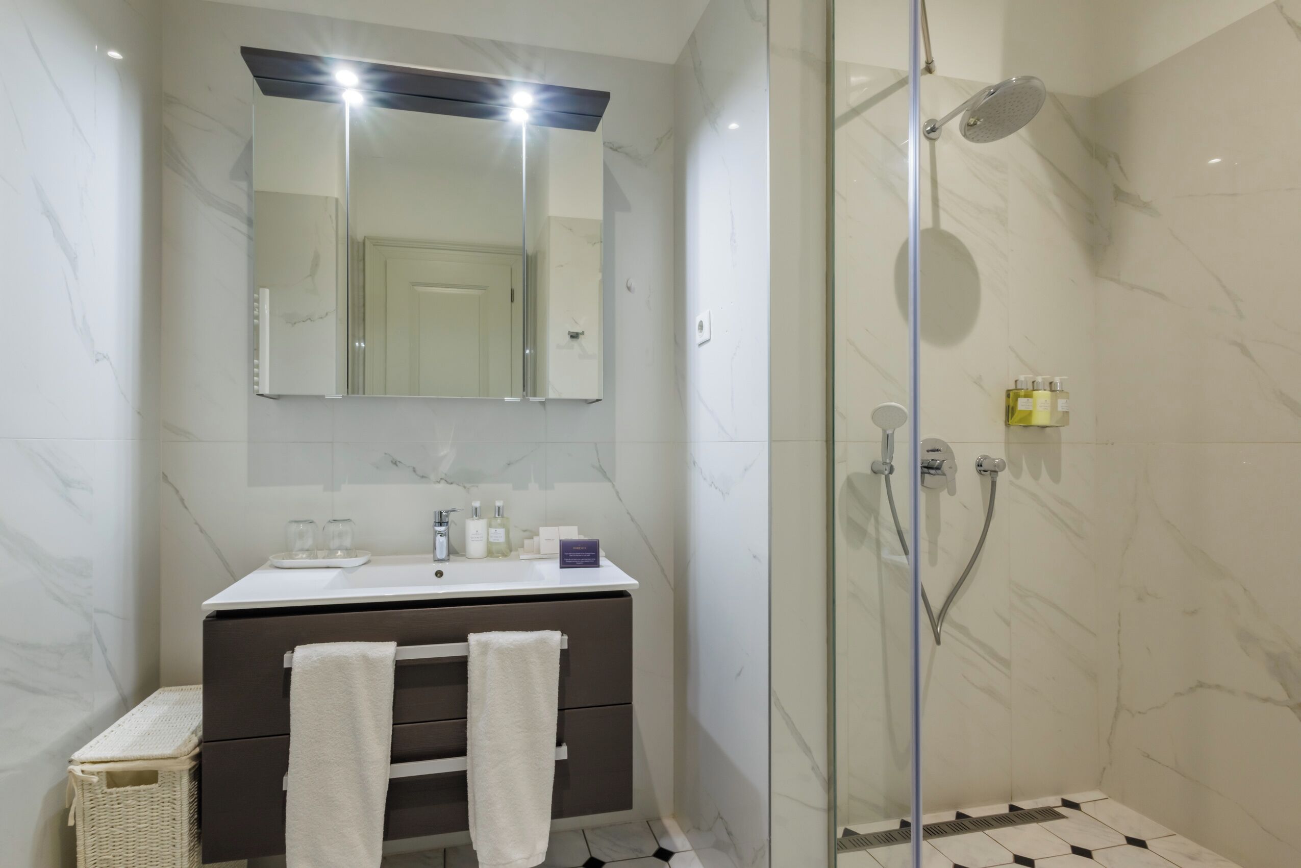 Un bagno moderno con doccia vetro, un mobile lavabo con specchio e pavimento piastrellato.