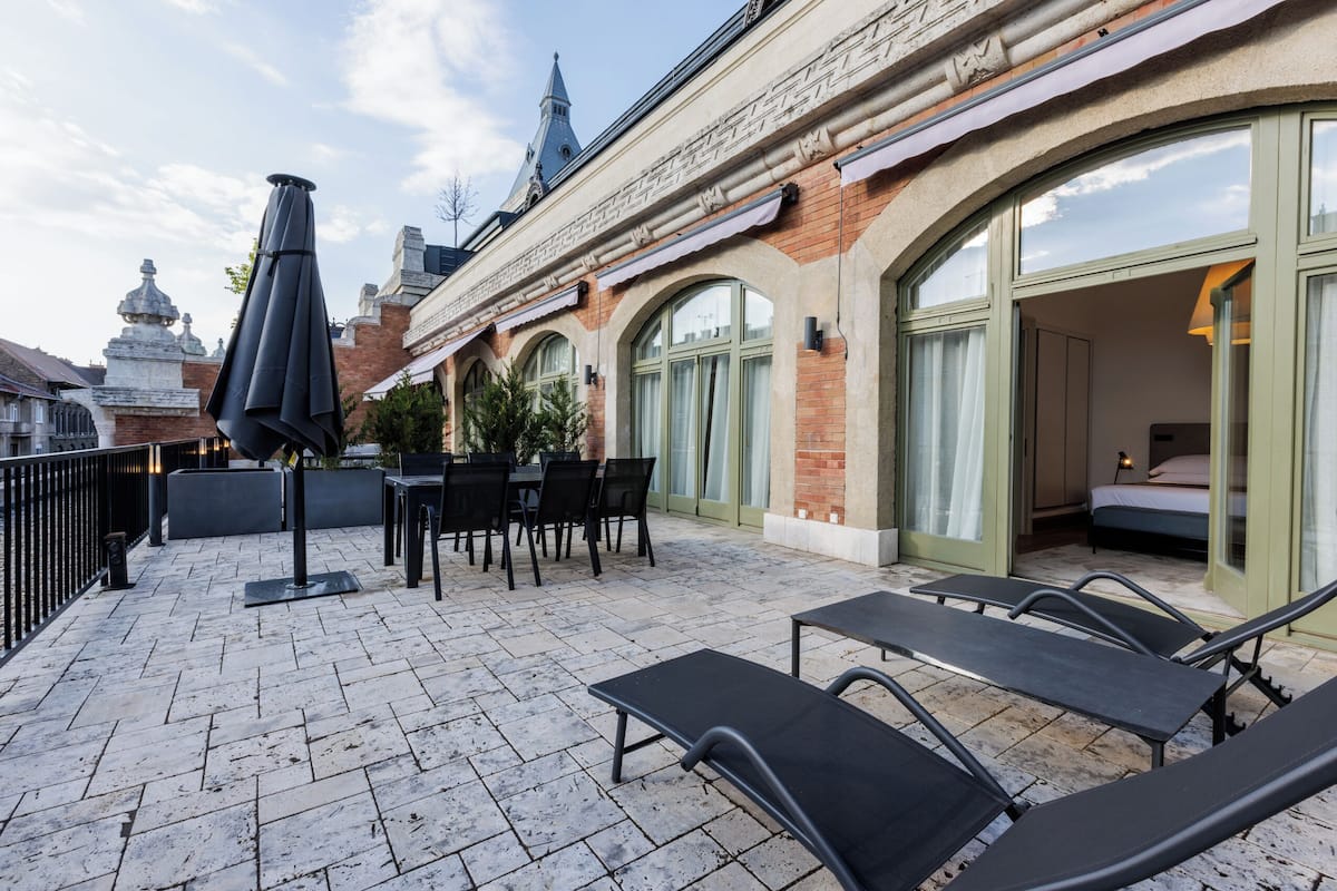 Terraza en la azotea con mesas al aire libre, zona de comedor y vistas a la aguja de una iglesia.