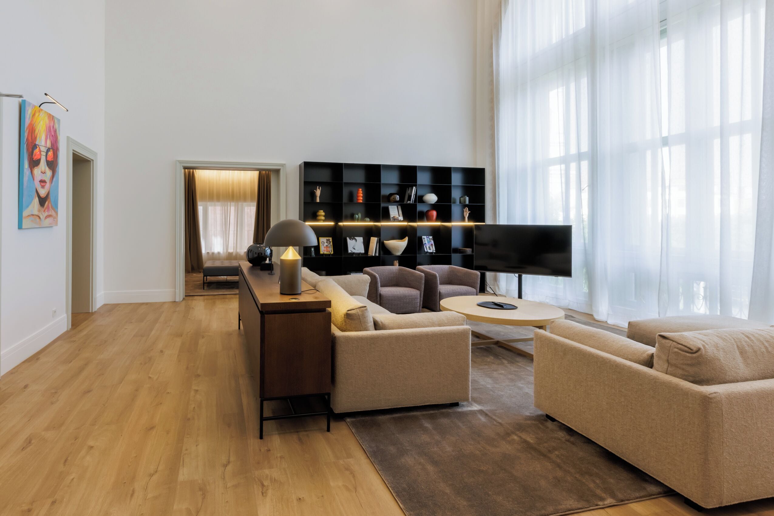 Un salon moderne avec un plancher en bois, un ensemble de canapés, un téléviseur et une étagère noire.