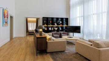 Un salon moderne avec un plancher en bois, un ensemble de canapés, un téléviseur et une étagère noire.