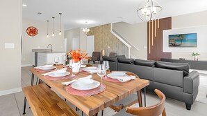 Ein moderner Essbereich mit einem Holztisch, gedeckt für vier Personen, einer grauen Couch und einer Treppe, die zu einer anderen Ebene führt.
