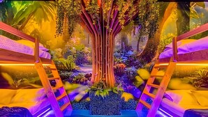A vibrant indoor garden with a central tree, surrounded by various plants and a small waterfall. - Modern Paradise on Windsor Cay: Luxurious 8BD Home (Clermont)
